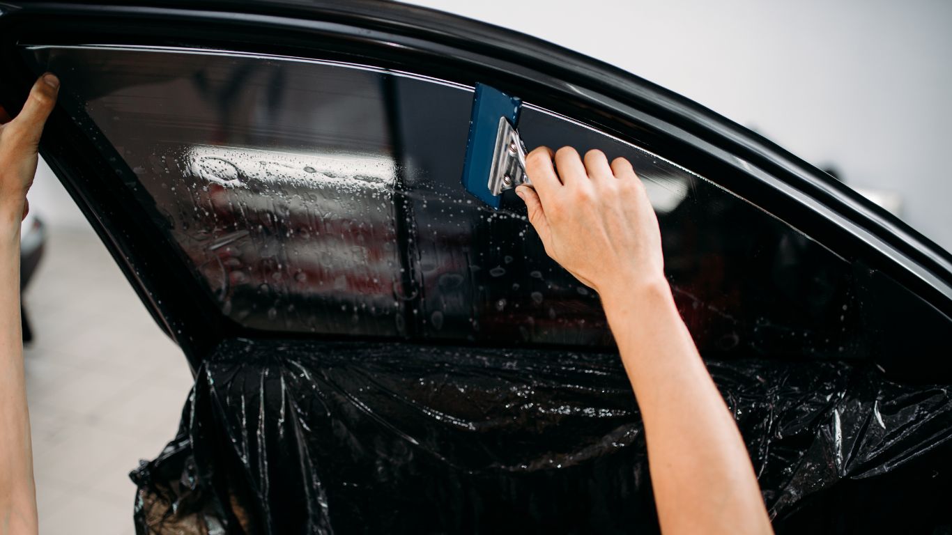 A person applying window tinting film to a car window for enhanced privacy and protection.